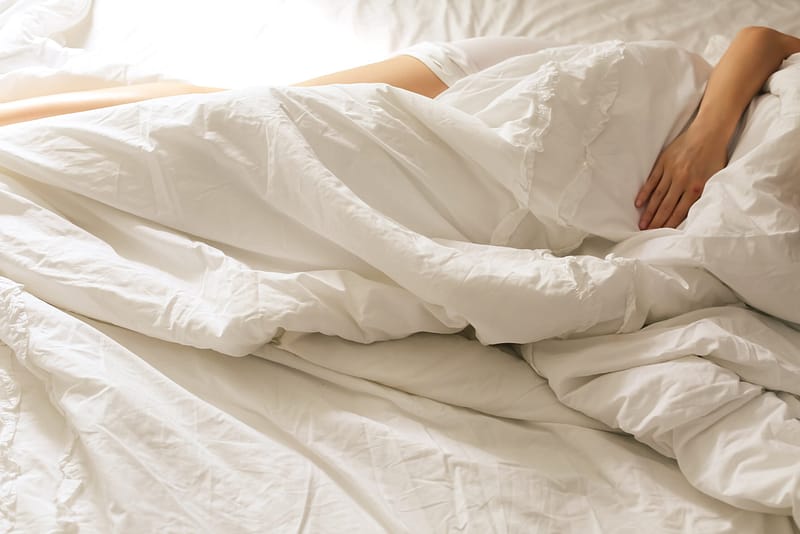 A person lying in a bed with white sheets